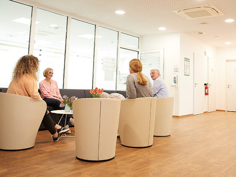 Vier Personen sitzen in der psychiatrischen Tagesklinik in Sesseln und unterhalten sich.