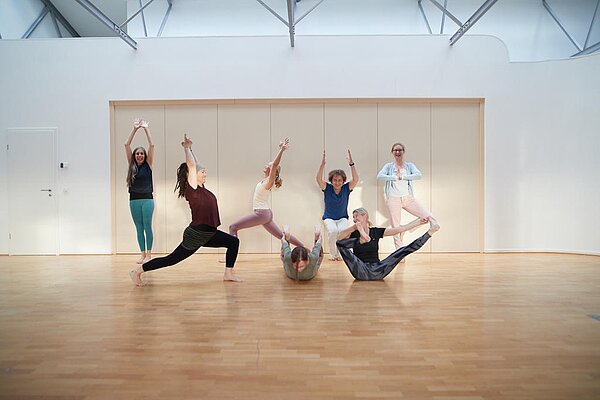 Eine Gruppe von Personen macht verschiedene Yoga-Übungen in einem Sportraum.