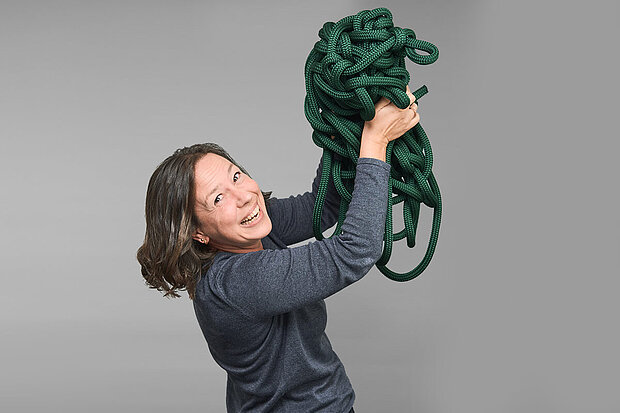 Eine Frau in einem grauen T-Shirt hält einen grünen Knüdel in die Luft..