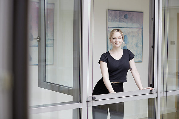 Eine lächelnde Frau lehnt sich an ein offenes Fenster der Institutsambulanz.