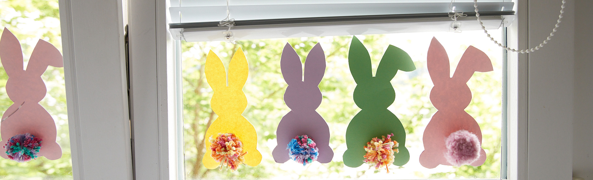 Bunte Papierhasen hängen in einer Kette am Fenster.