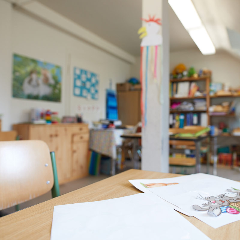 Ein Klassenraum der Klinikschule mit Fokus auf einen Schreibtisch mit Stuhl, auf dem zwei Zettel liegen.