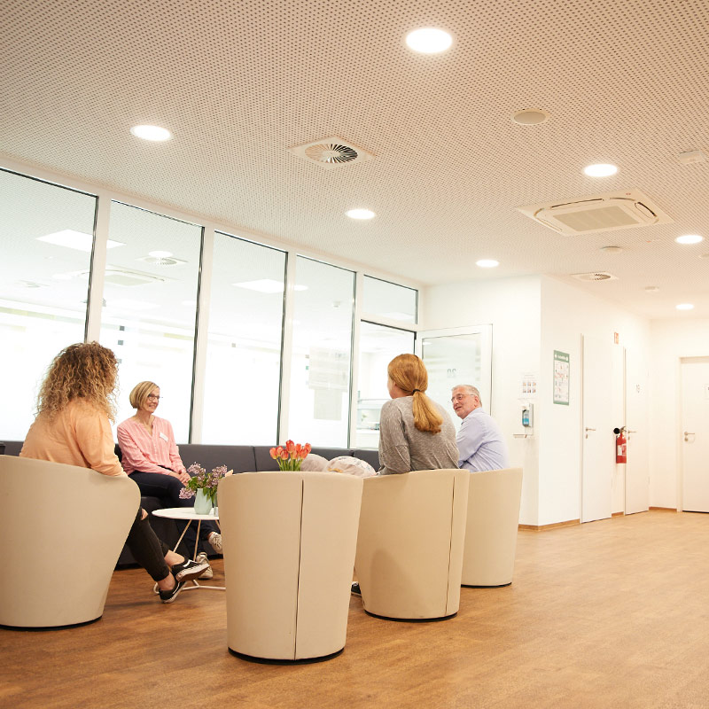 Vier Personen sitzen in der psychiatrischen Tagesklinik in Sesseln und unterhalten sich.