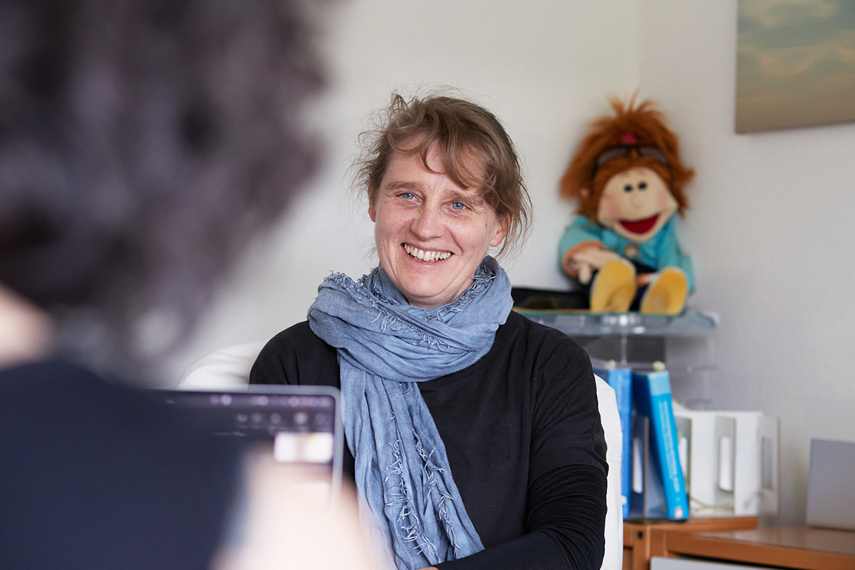 Zwei Personen befinden sich im Gespräch, der Fokus liegt auf einer lächelnden Frau.