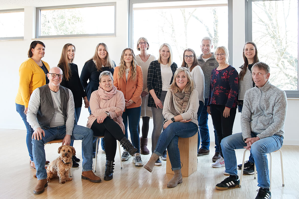Eine Gruppe von Personen und einem Hund steht und sitzt in einem Raum des Tagesklinik und lächelt in die Kamera.