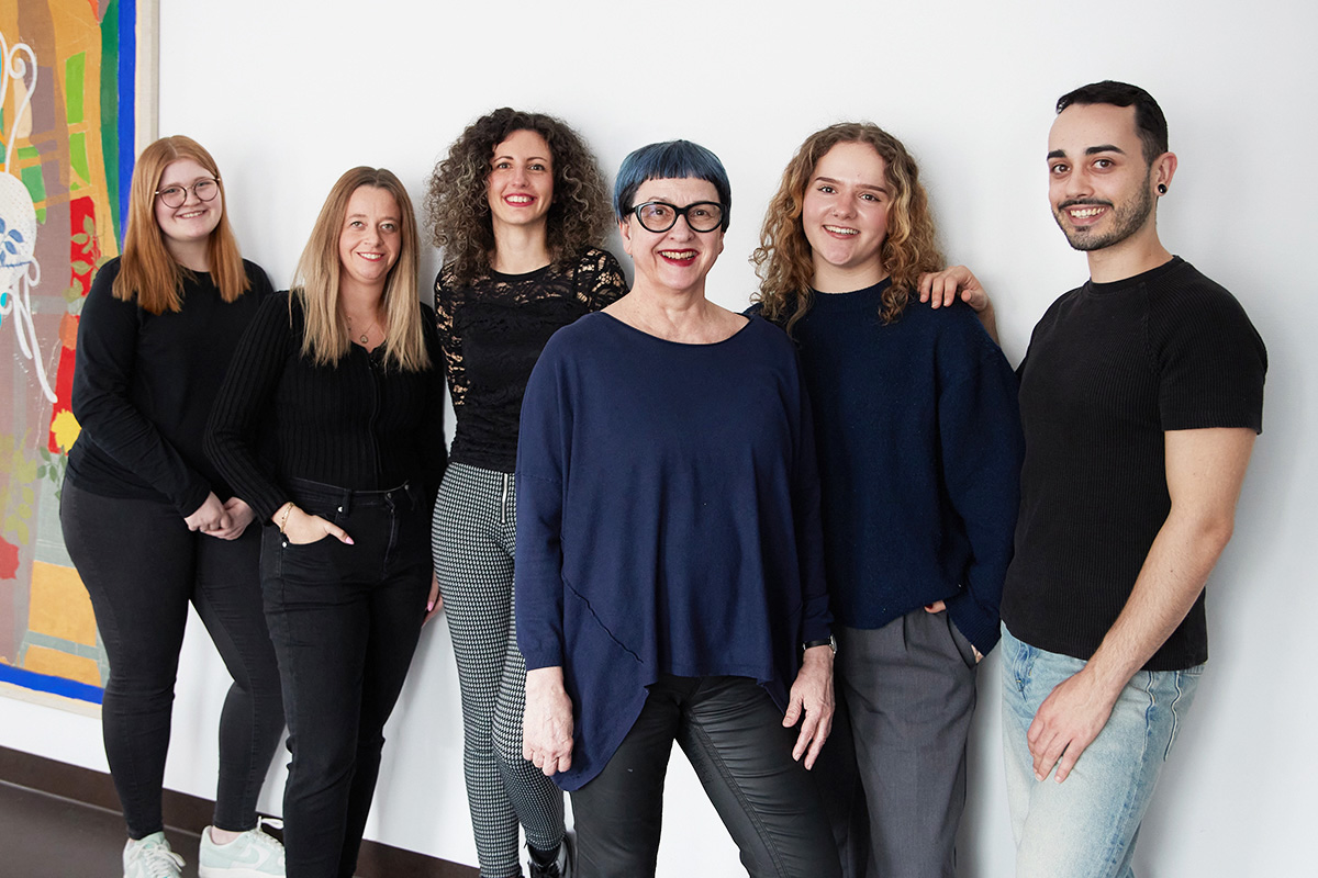 Sechs Personen stehen in einem Raum und lächeln in die Kamera.